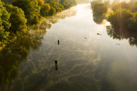 aerial shot of a man fly fishing in a river during summer morning